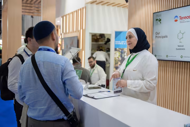 Finan Group team member speaking with a visitor at the stand reception desk, Gulfood Manufacturing 2024